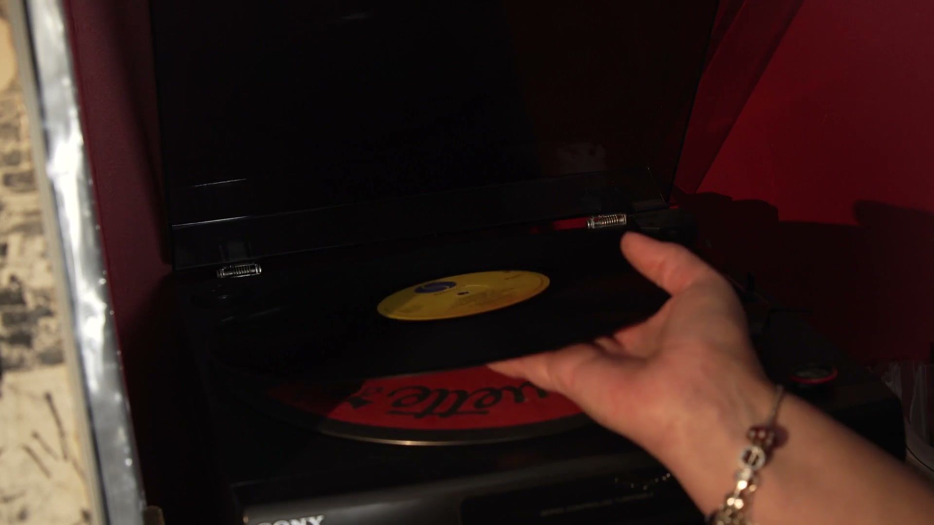 Low-key close-up of a hand with a bracelet placing a vinyl record on a turntable. (opens a larger view)