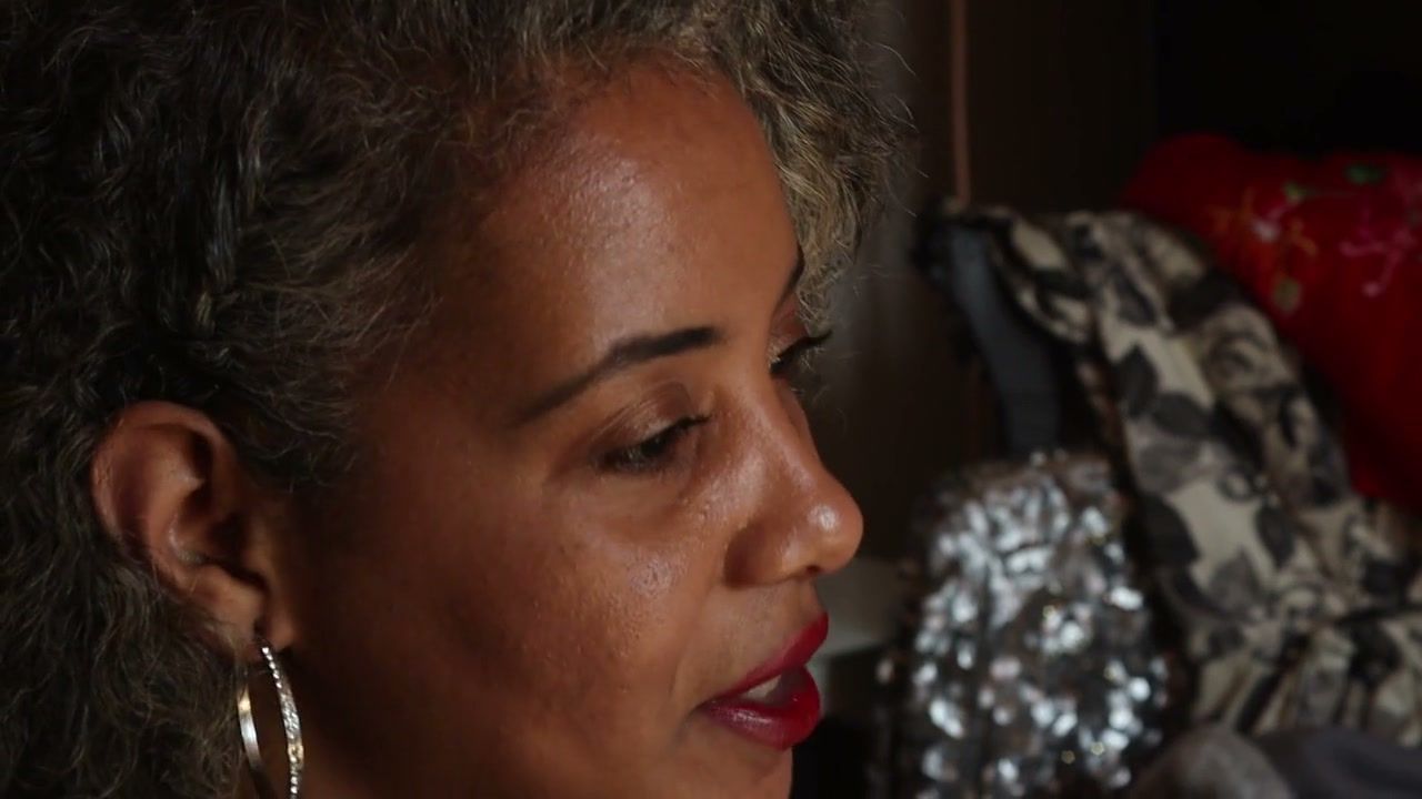 Tight profile of Dixie looking down, with a hoop earring and red lipstick; sequins and embroidered fabric out of focus behind her. (opens a larger view)