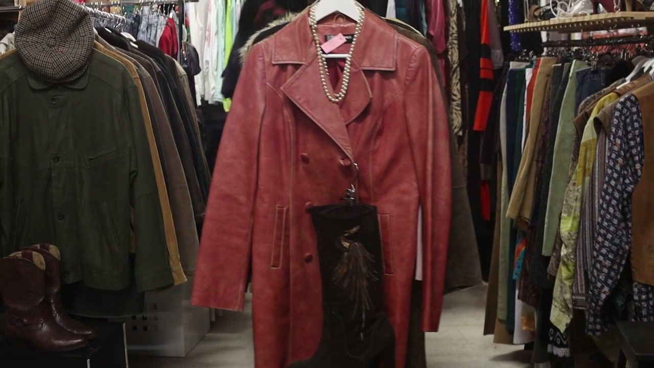 A faded red leather coat with pearls and a cowboy boot on a market rail, surrounded by racks of vintage clothes. (opens a larger view)