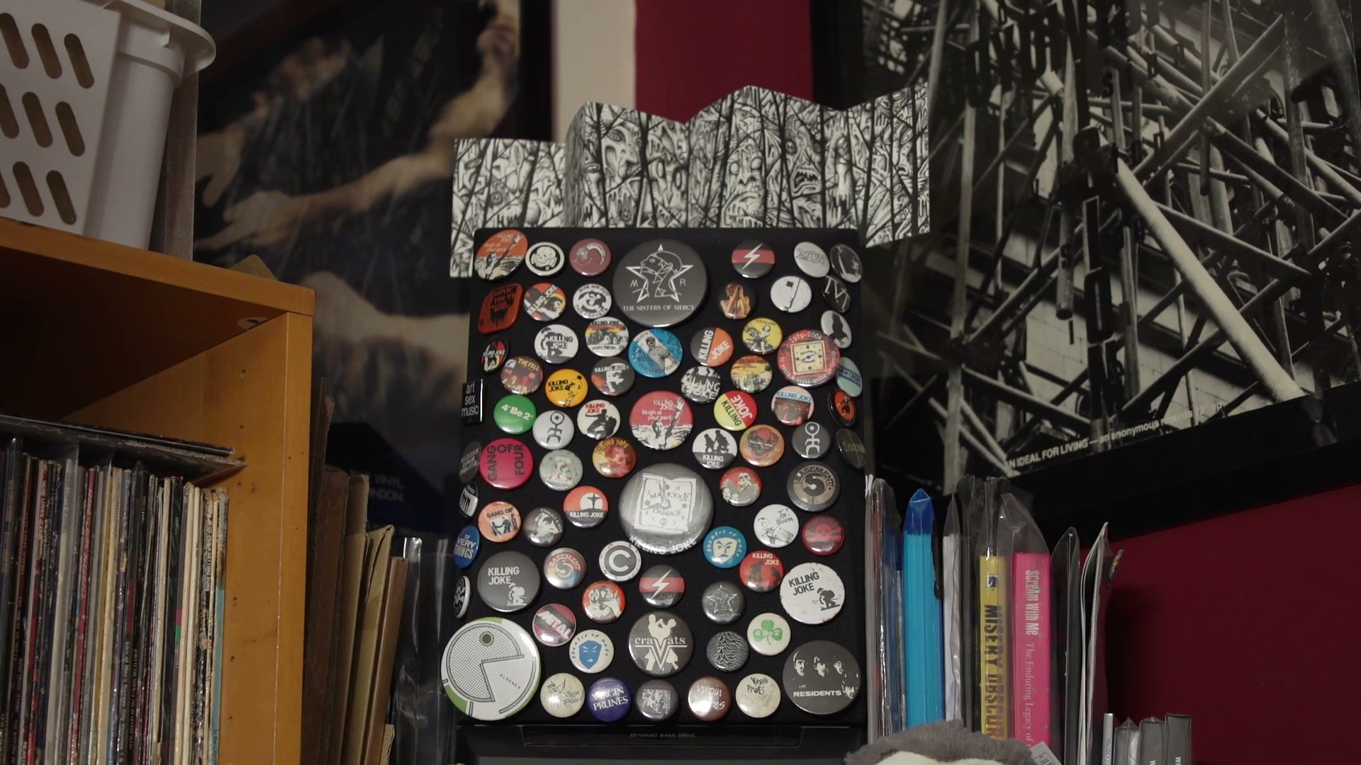 A board covered in punk band badges beside shelves and a framed print.