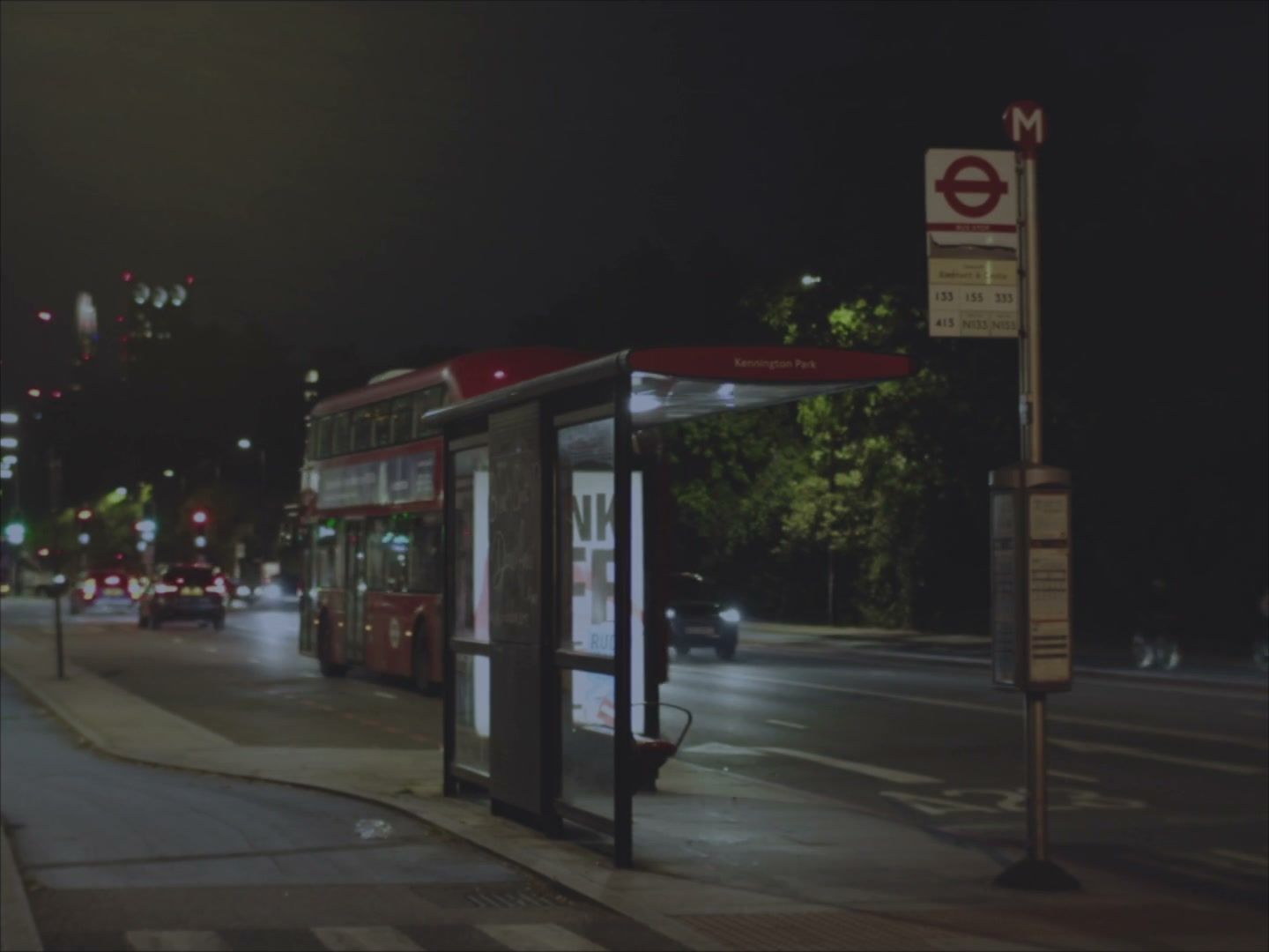 Establishing shot of an empty London bus stop at night, a red double-decker pulling away. (opens a larger view)